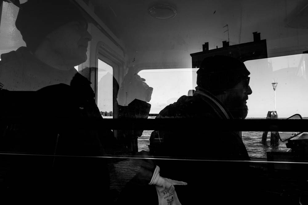 Potente fotografia in bianco e nero con riflessi e silhouette che si sovrappongono realizzata nella cabina di pilotaggio di un vaporino di Venezia