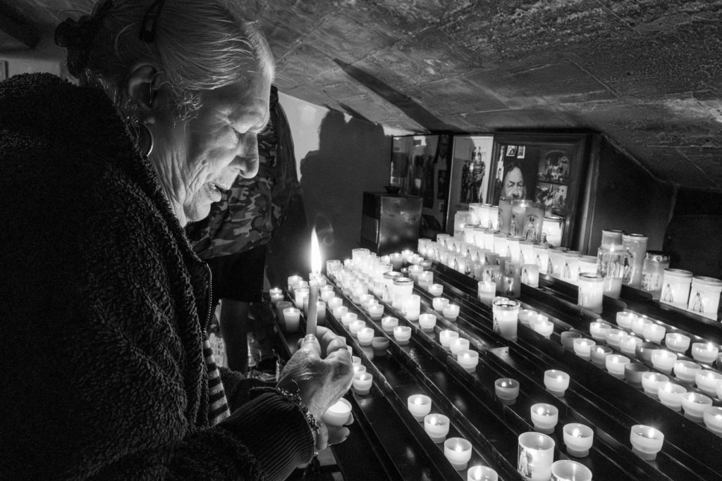 Anziana donna Rom in preghiera davanti ad un altare in un potente Bianco e Nero